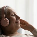 Happy older woman in big headphones resting on comfortable couch